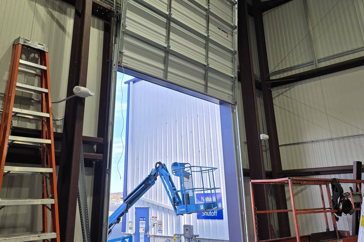 Large commercial sectional door installed in a steel building, with ladder and lift on site