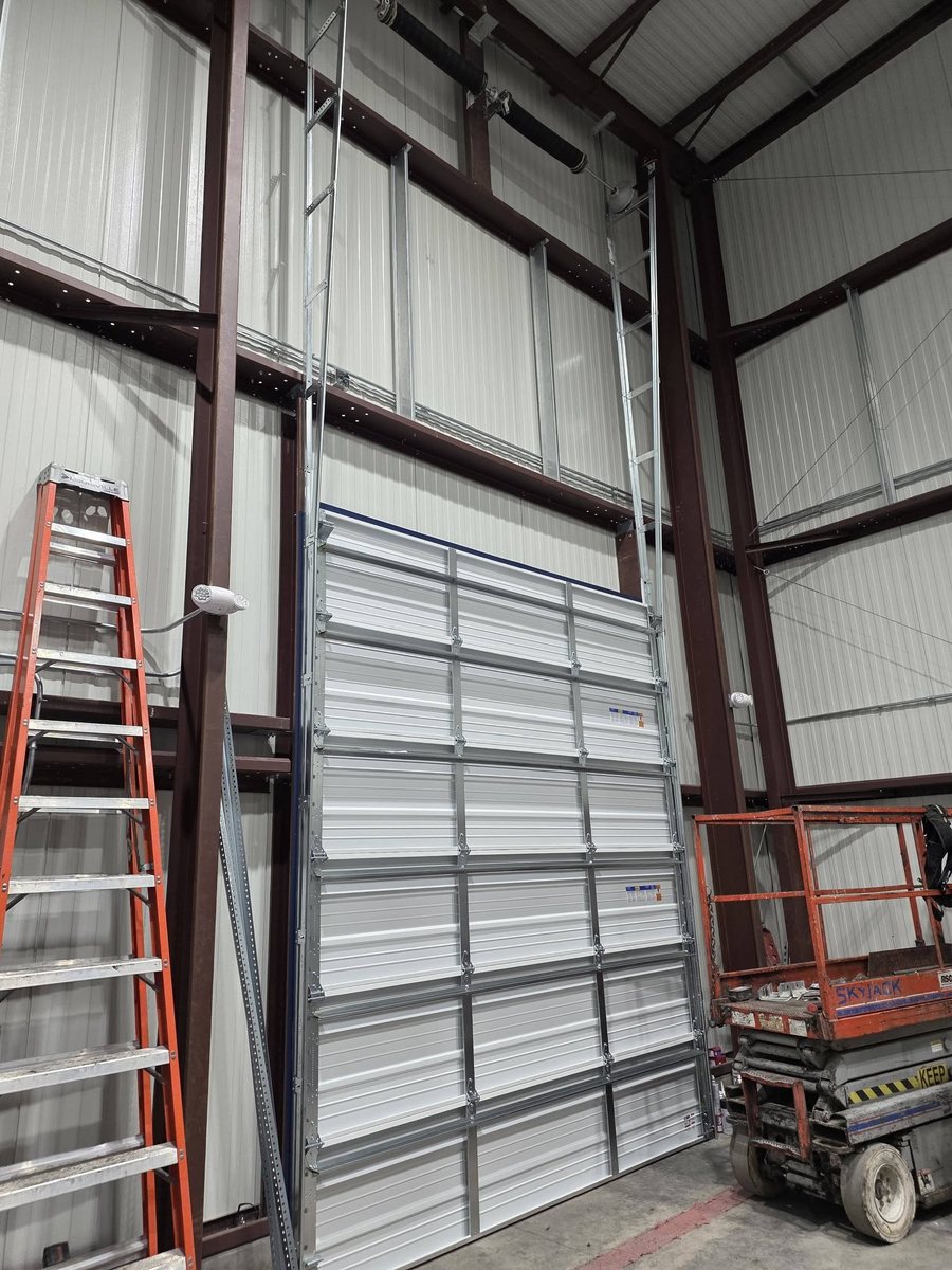 Large commercial overhead door going in, with ladder and scissor lift on site