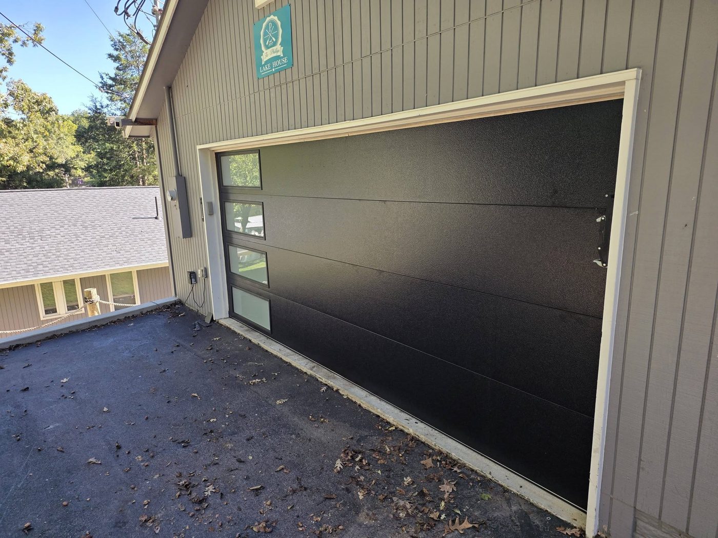 New black modern garage door with a vertical glass strip, installed at a lake house